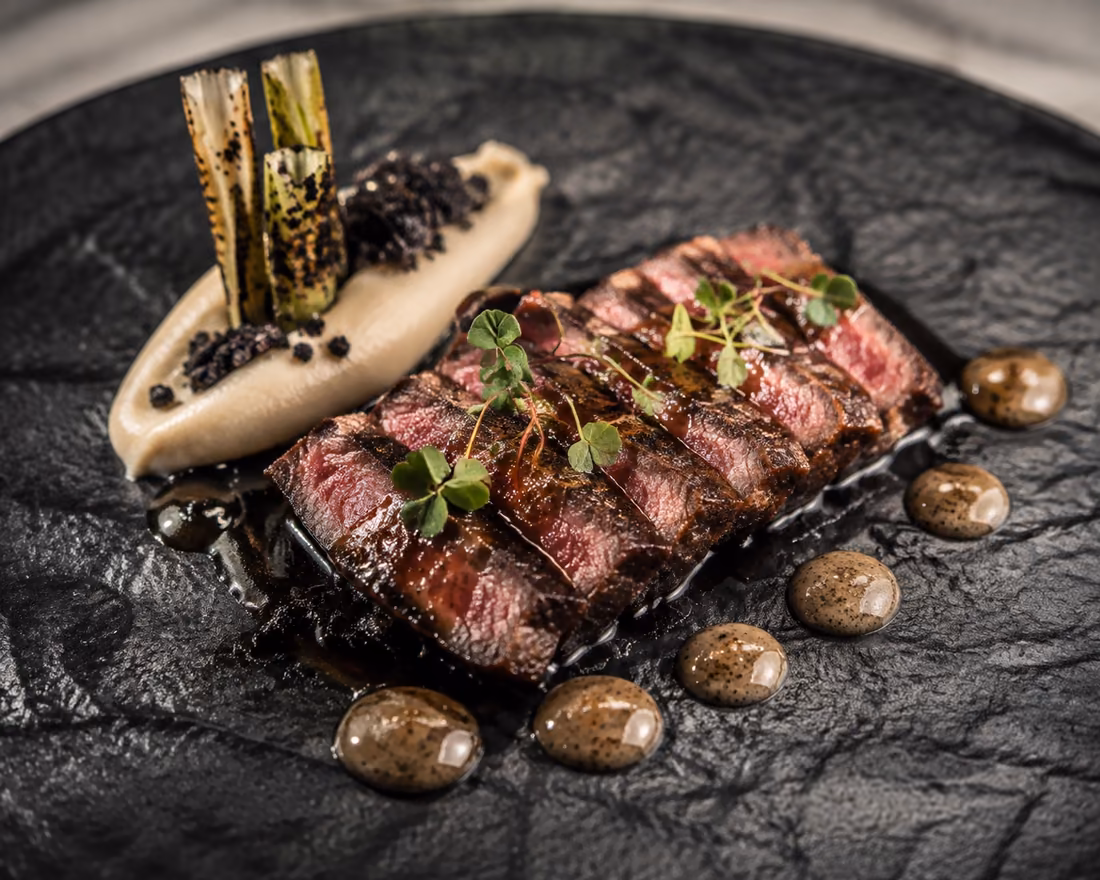 Sliced charcoal grilled beef with grilled leek and smoked cream on slate